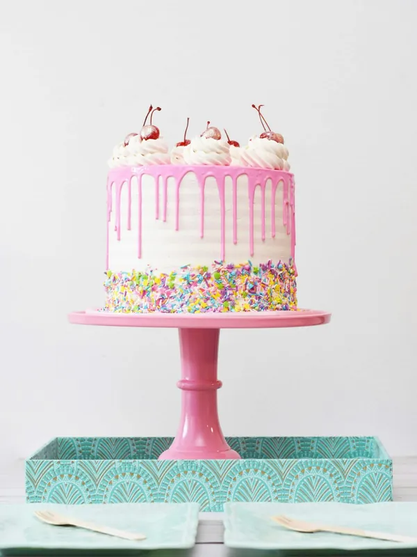 A pink drip birthday cake with sprinkles on a cake stand